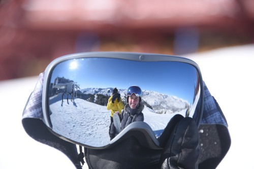 Picture of Bridget holding a pair of ski goggles, and you can see her reflection in the lens.